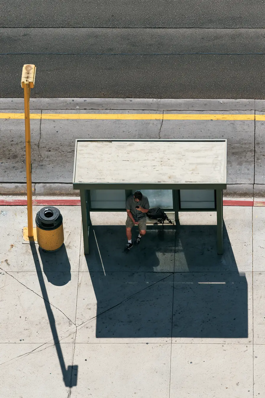 Man smiling at an approval notification while waiting at a sunny bus stop
